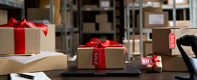 Table with laptop and gift boxes with sale tags on table in warehouse.