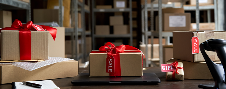 Table with laptop and gift boxes with sale tags on table in warehouse.