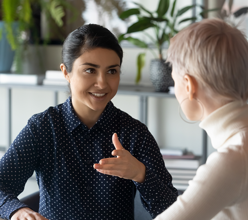 796×705 logistics Friendly millennial businesswoman talking to blonde female colleague, sitting at table in office.