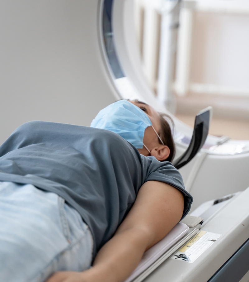 A woman in a medical mask lies on the tomograph table.
