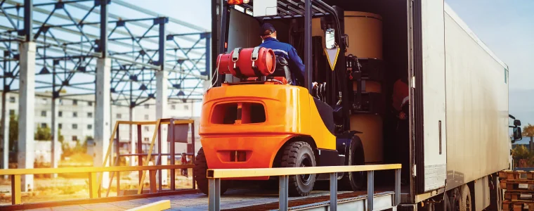 Forklift is putting cargo from warehouse to truck outdoors